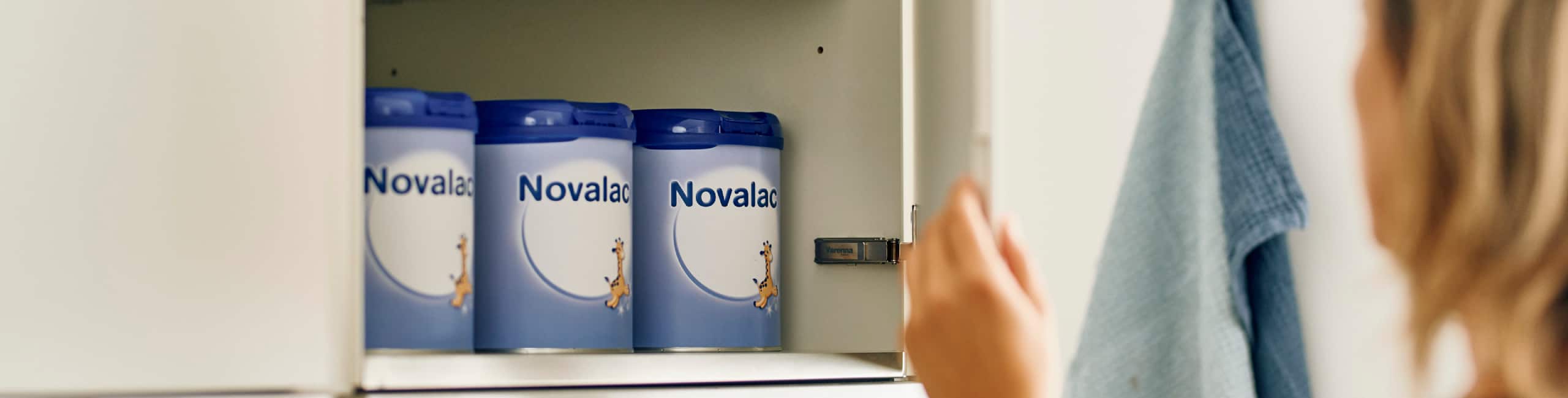 Mamica sega po Novalac formulah, ki so zložene na kuhinjski polici