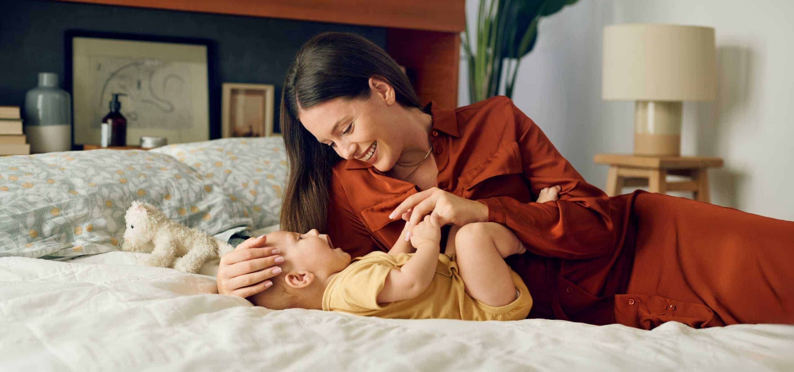 Mamica se igra z dojenčkom na postelji.